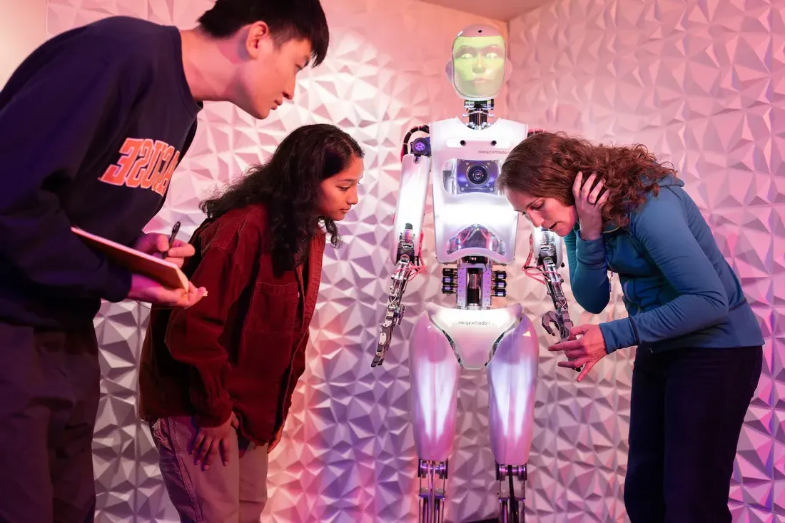 Three students observing a robot in an exhibit.